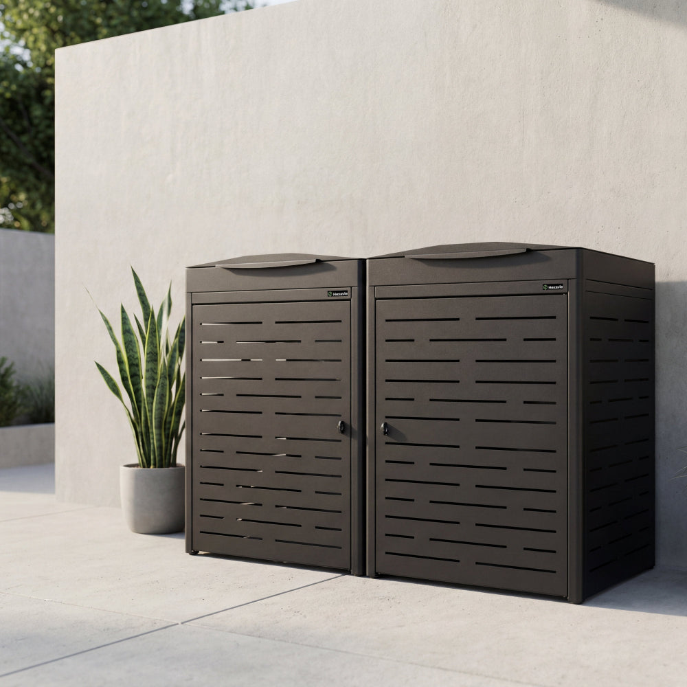 Two brown outdoor trash cans against a light stone wall with a plant in the background.