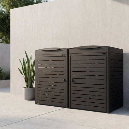 Two brown outdoor trash cans against a light stone wall with a plant in the background.