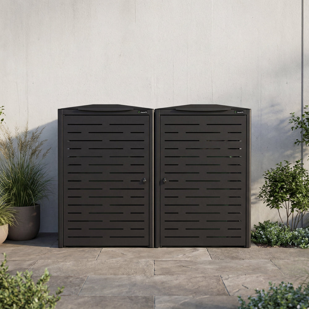 Two black outdoor storage units against a light gray wall with plants around.
